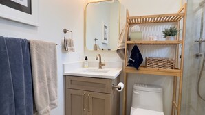 Ein Badezimmer mit Waschbecken, Spiegel, Toilette und einem Holzboden mit Pflegeprodukten.