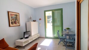 A living room with a TV, a white cabinet, a painting, and a dining area with blue chairs and a table.