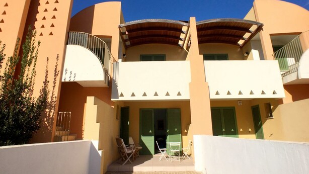 A building with a curved roof, balconies with railings, and green shutters.