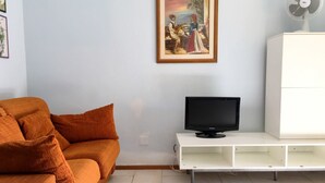 A living room with a sofa, a television on a stand, a white cabinet, and a painting on the wall.