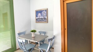 A small dining area with a table and four chairs, a potted plant on the table, and a framed picture on the wall.