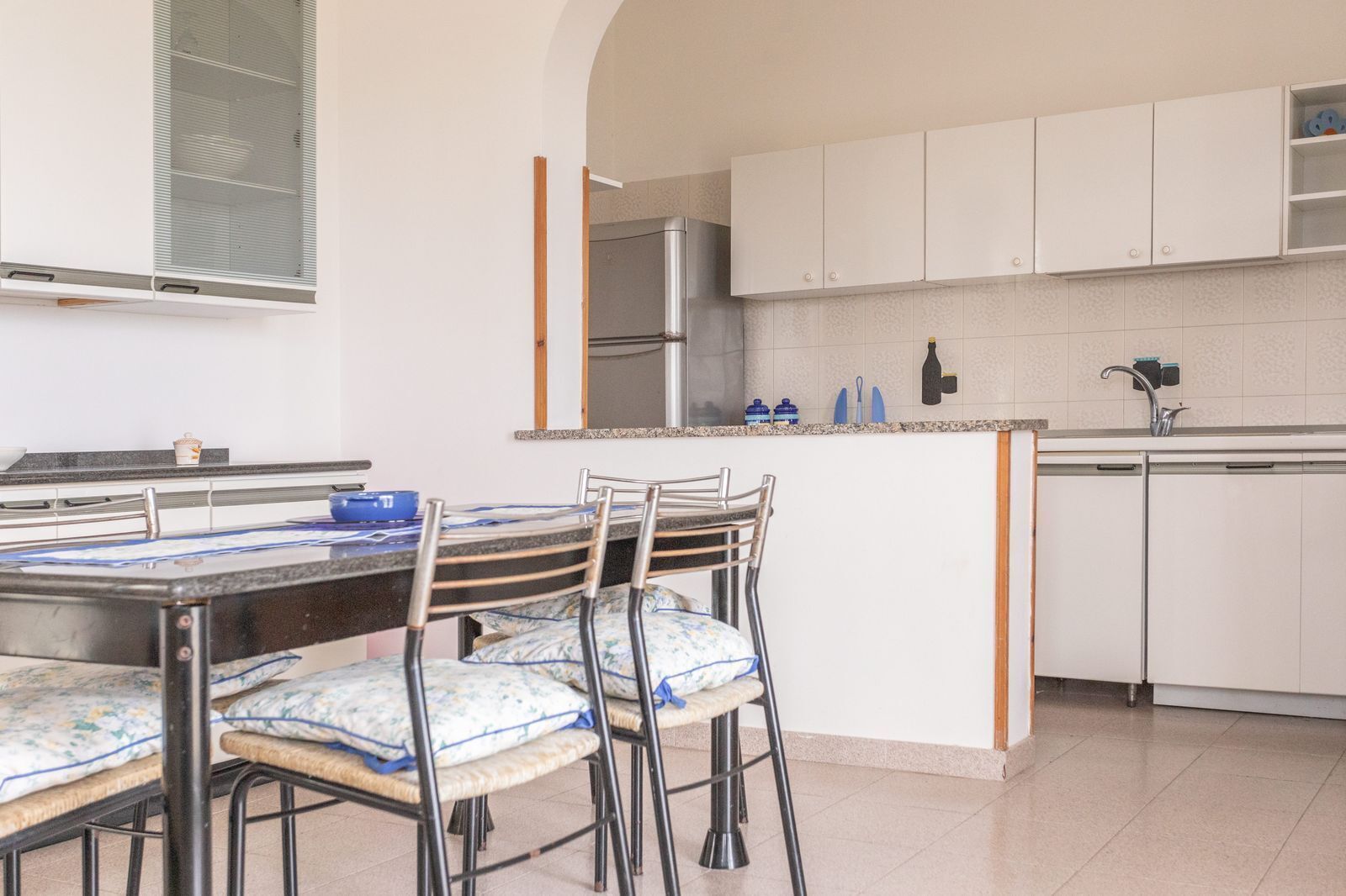 Een moderne keuken met witte kastjes, een roestvrijstalen koelkast en een eethoek met een tafel en stoelen.