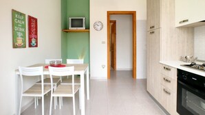 A modern kitchen with white cabinets, a built-in oven, and a dining area with a table and chairs. - Villetta Iris (Morciano di Leuca)