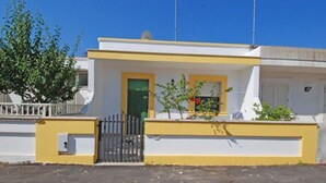 A modern building with a yellow and white facade, a gated entrance, and a small garden area with plants and flowers. - Villetta Iris (Morciano di Leuca)