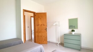 A bedroom with two beds, a wooden door, a white radiator, a green dresser, and a framed picture on the wall. - Villetta Iris (Morciano di Leuca)