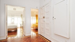 Een gang met houten vloer, witte muren en een bed in de aangrenzende kamer.