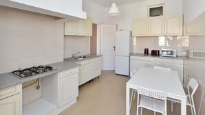 Een moderne keuken met witte kasten, een gasfornuis, een magnetron en een eettafel met stoelen.