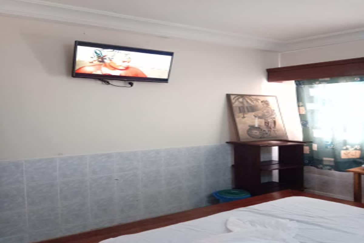 A hotel room with a bed, a television mounted on the wall, a small wooden table, and a window with curtains.