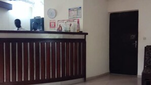 Een receptiegedeelte met een houten balie, een zwarte deur en een muur met een klok en wat berichtjes.
