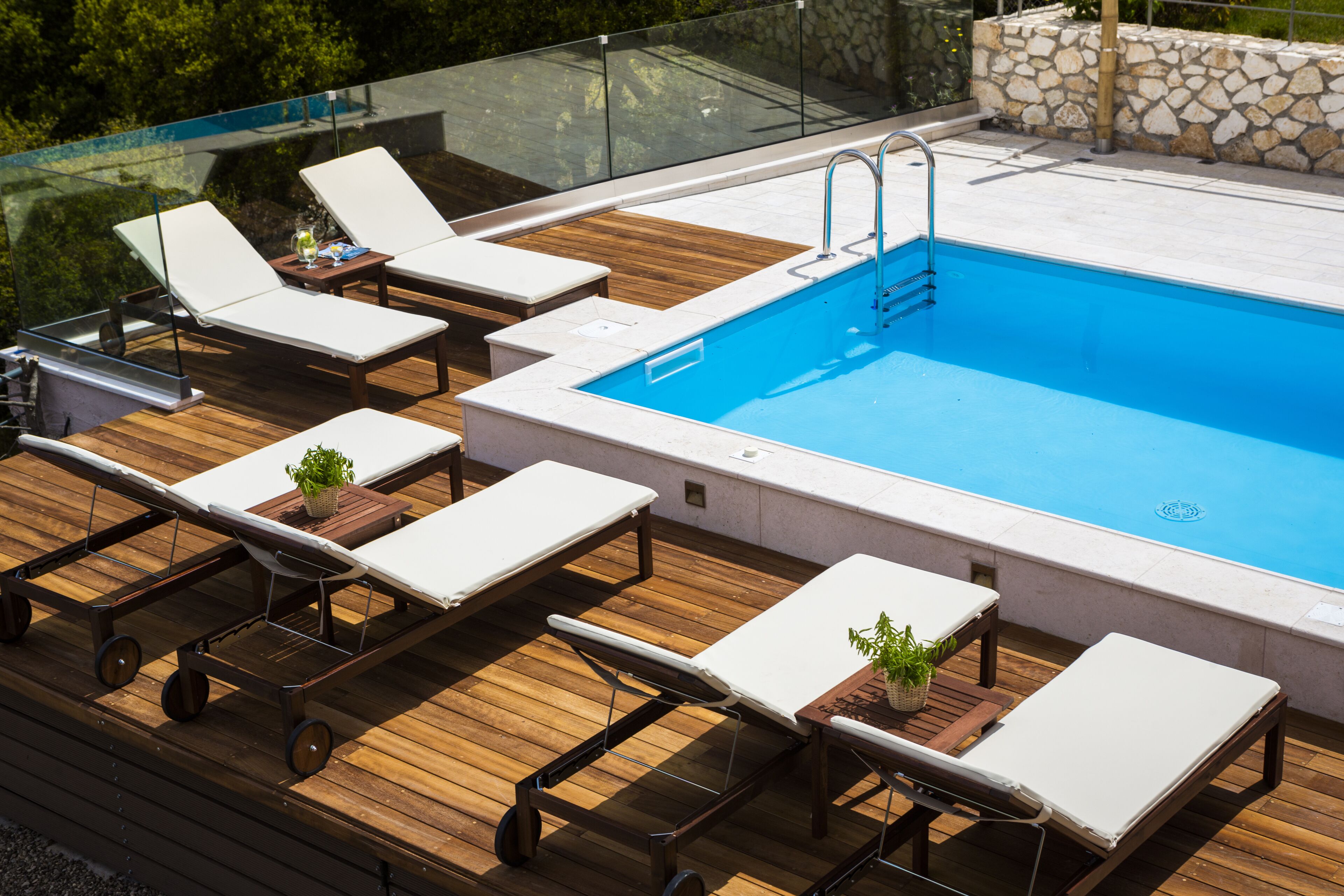 A poolside area with lounge chairs, a small table with a plant, and a stone wall in the background.