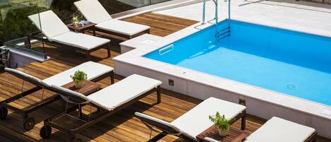A poolside area with lounge chairs, a small table with a plant, and a stone wall in the background.