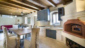 A kitchen with wooden beams, a dining table, chairs, cabinets, and a wood-fired oven. - Iconic Villas, Villa Rosa with private pool and stunning mountain view (Drakopoulata)