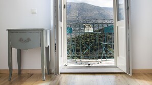 A room with a wooden floor, a small table, and a door leading to a balcony with a view of mountains and a metal fence. - Iconic Villas, Villa Rosa with private pool and stunning mountain view (Drakopoulata)