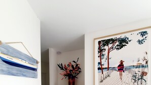 A hallway with a wooden cabinet, a framed painting of a beach scene, and a blue-striped wall hanging.