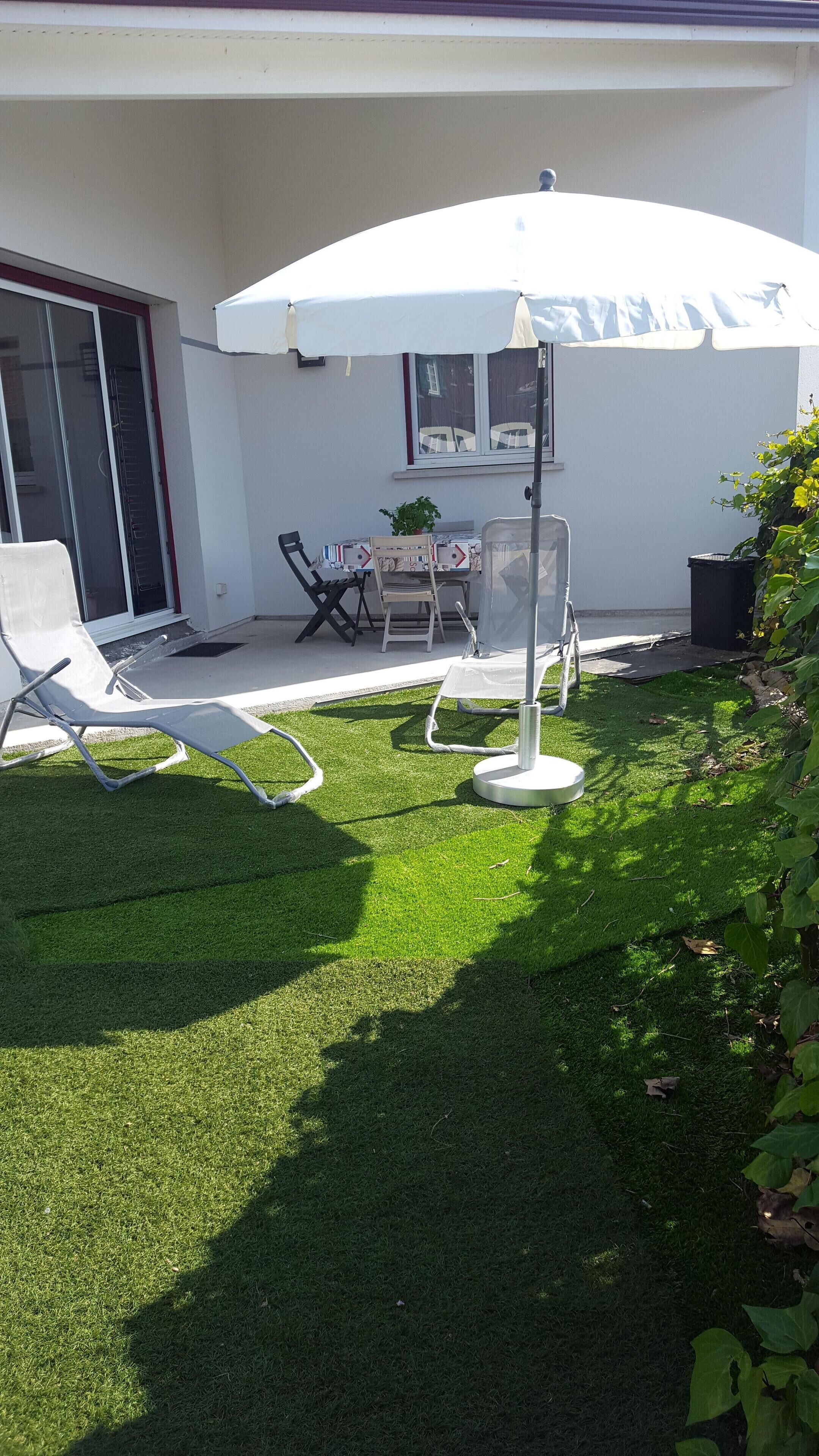 A patio area with a white umbrella, a table with chairs, and a small garden.