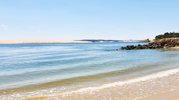 A beach with clear blue water, sandy shore, and rocky outcrops.