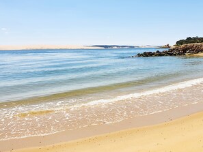 Une plage avec une eau d’un bleu limpide, un rivage sablonneux et des affleurements rocheux.