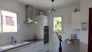 A modern kitchen with white cabinets, a stainless steel range hood, a built-in oven, a window, and a small dining area with a bench.