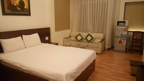 A hotel room with a large bed, a sofa, a glass table, a refrigerator, and a chair. - Classic Room- Free Laundry Services in District 1 (District 1)