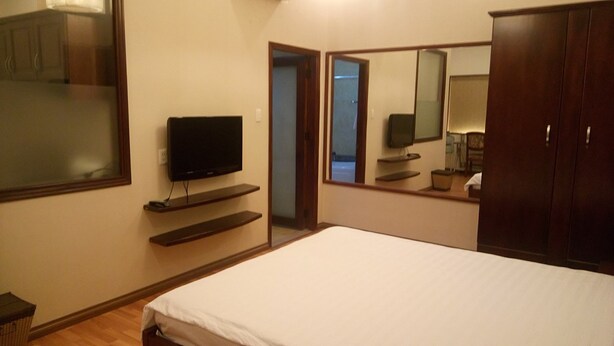 A bedroom with a bed, a TV on a shelf, a wardrobe, and a mirror. - Classic Room- Free Laundry Services in District 1 (District 1)