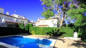 Une piscine dotée d’une terrasse carrelée, entourée d’une haie bien entretenue et d’un grand arbre.