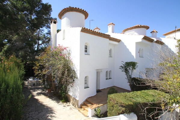 A white building with a courtyard, stone pathway, and a small table with chairs.