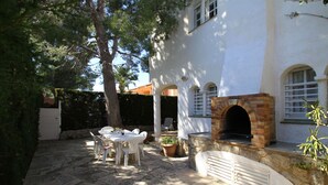 Un espace patio avec une table et des chaises en pierre, un four en briques et un bâtiment blanc doté de fenêtres en arc de cercle.