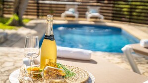 A bottle of champagne, a glass, and a plate with snacks on a table by a pool.