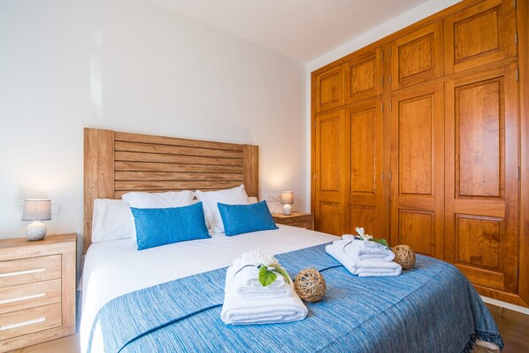 A neatly made bed with blue and white bedding, wooden headboard, and a large wooden wardrobe.