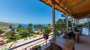 A wooden deck with tables and chairs overlooking a beach and sea. - Hotel Bahamas (Sarandë)