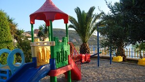 A playground with a slide and climbing structures, surrounded by sand and palm trees. - Hotel Bahamas (Sarandë)