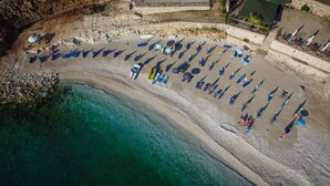 An aerial view of a beach with rows of umbrellas and lounge chairs, clear turquoise water, and a rocky shoreline. - Hotel Bahamas (Sarandë)