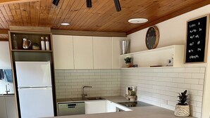 Una cucina moderna con soffitto in legno, mobili bianchi, una grande isola con sgabelli e una lavagna con una citazione motivazionale.