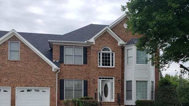 A two-story brick house with a front entrance, a garage, and a well-maintained lawn with yellow flowers. - Amazing W Marietta 5BR-3BA Relocation, Long Stay (Marietta)