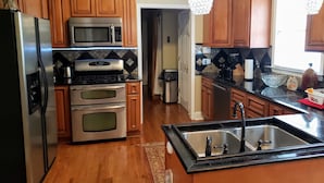 A kitchen with wooden cabinets, stainless steel appliances, a black countertop, and pendant lights. - Amazing W Marietta 5BR-3BA Relocation, Long Stay (Marietta)