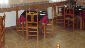 Un comedor con varias mesas dispuestas para una comida, sillas de madera y piso de baldosas.