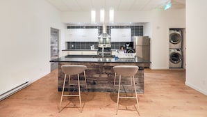 A modern kitchen with a central island, bar stools, a built-in oven, and a washing machine. - HoMa HomeStay Hotel by Olympic Stadium Montreal (Auberge/Hostel) (Montreal)
