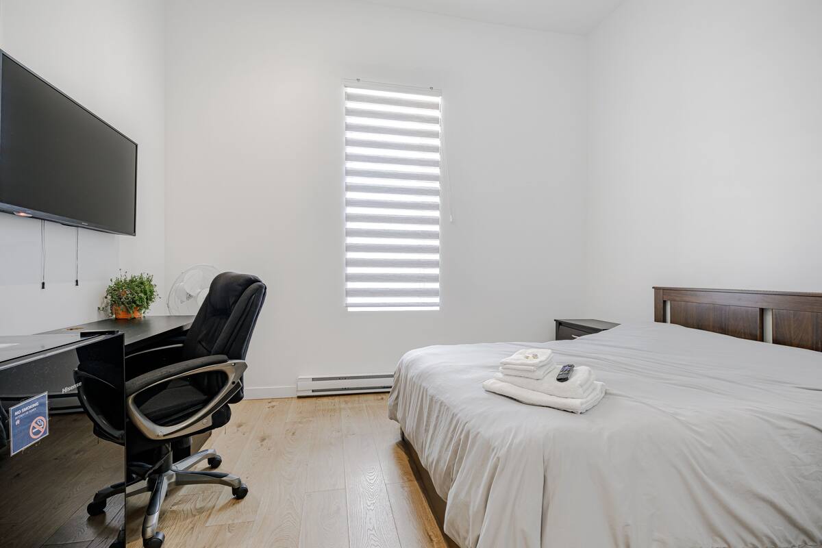Habitación de hotel con cama, escritorio con computadora, silla, televisor y ventana con persianas.