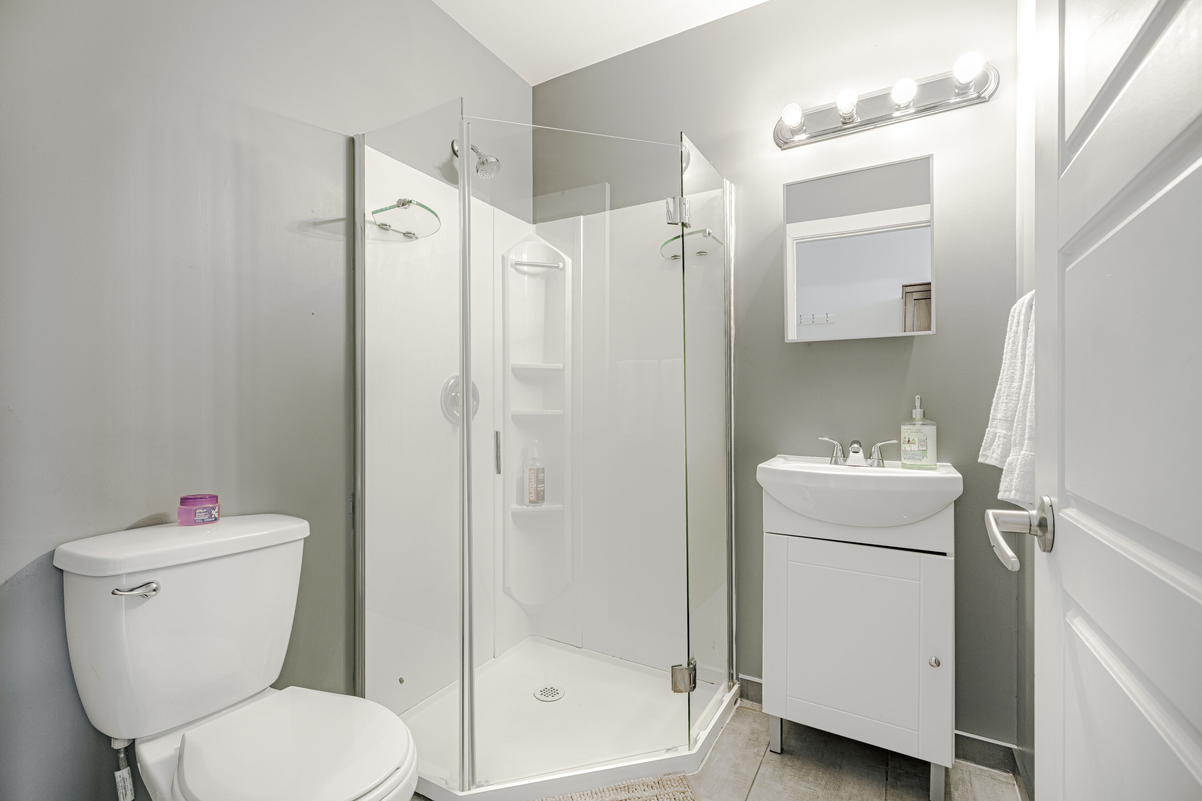 A bathroom with a toilet, a glass-enclosed shower, a sink, and a mirror with lights.