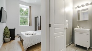 A bedroom with a bed, a potted plant, a window, and a door leading to a bathroom with a sink and mirror. - HoMa HomeStay Hotel by Olympic Stadium Montreal (Auberge/Hostel) (Montreal)