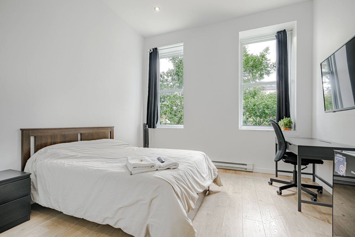 Un dormitorio con una cama, un escritorio y dos ventanas.