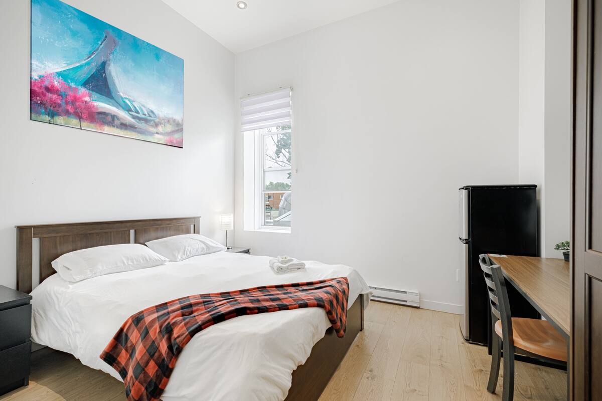 Una habitación de hotel con cama, escritorio, silla, un cuadro y ventana.