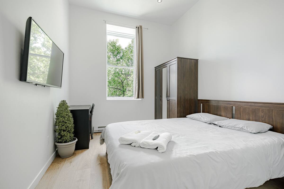 Un dormitorio moderno con una cama grande, un televisor de pantalla plana montado en la pared, una planta en maceta y un armario.