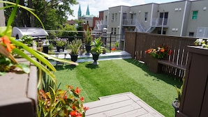 A backyard with artificial grass, potted plants, a barbecue grill, and a wooden deck. - HoMa HomeStay Hotel by Olympic Stadium Montreal (Auberge/Hostel) (Montreal)