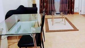 Un comedor con una mesa de vidrio y sillas, una mesita de madera y un jarrón decorativo.