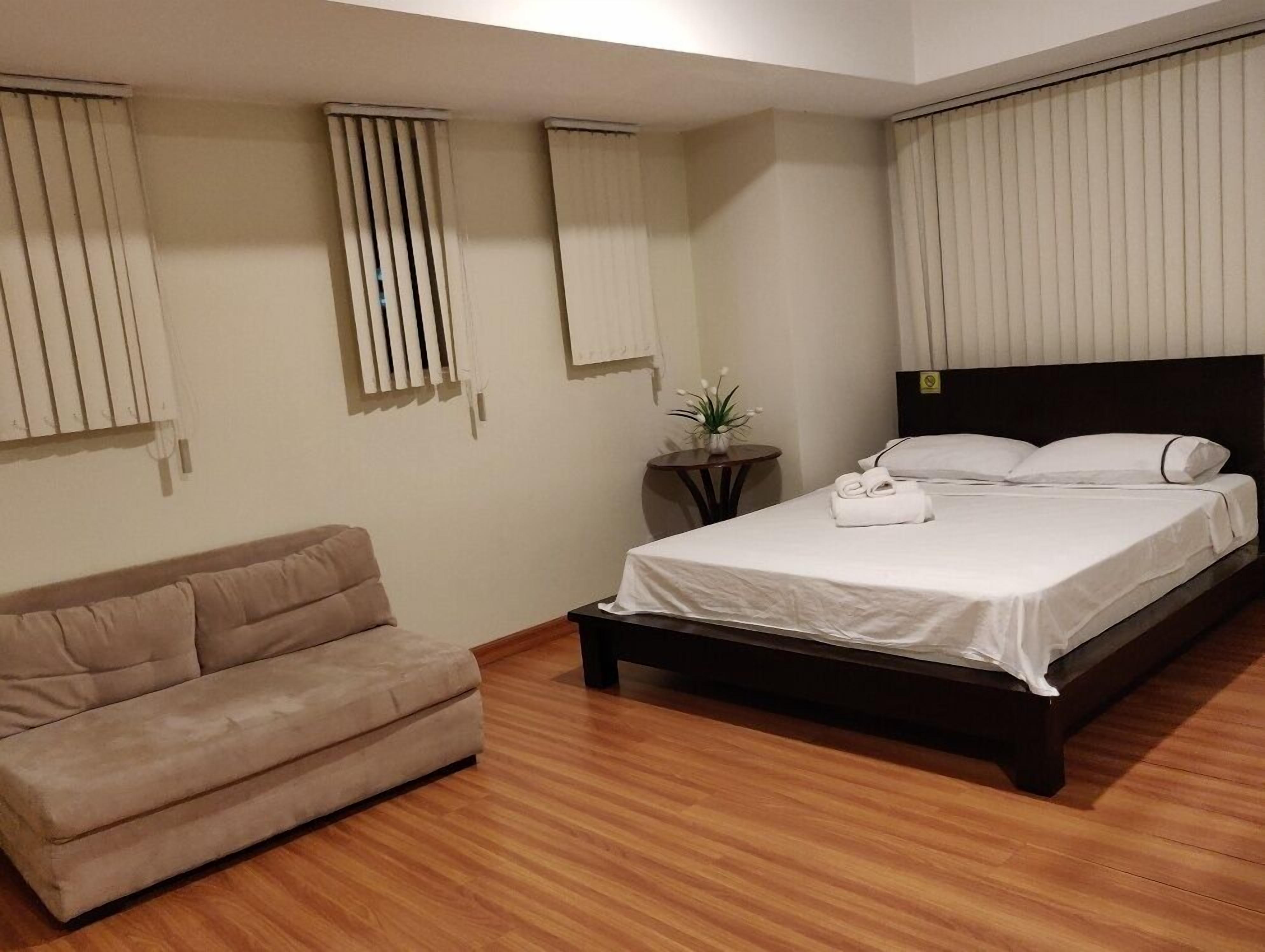 A bedroom with a bed, a sofa, a small table with a plant, and a mirror on the wall.