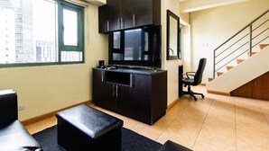 Una cocina compacta con armarios oscuros, un microondas integrado y una pequeña encimera. Se observa una silla de oficina negra y una escalera que conduce a otro nivel.