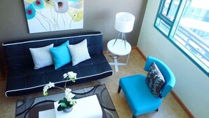 Un salón moderno con un sofá negro, un sillón azul, una mesa blanca y un cuadro en la pared.