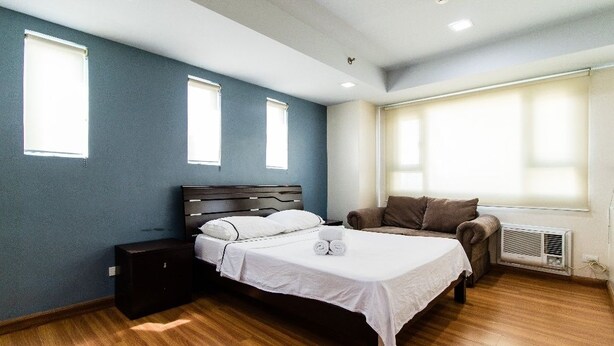 Un dormitorio con cama, mesitas de noche, una silla y una ventana.