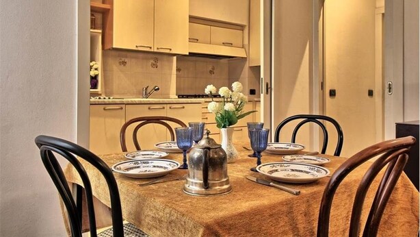 A dining area with a table set for four, surrounded by wooden chairs. A vase with white flowers is on the table. - Logicasa Residenza Como Centro (Como)